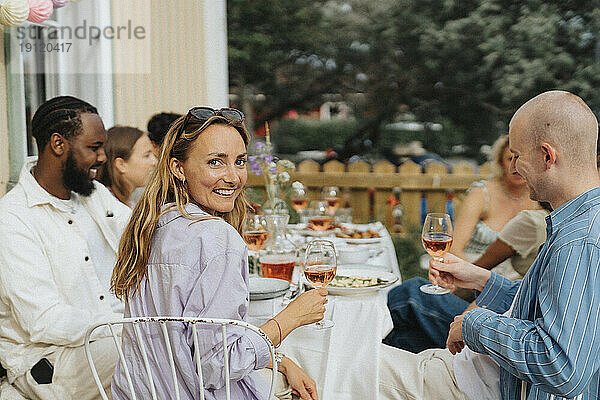 Porträt einer lächelnden jungen Frau  die über die Schulter schaut  während sie mit Freunden bei einer Dinnerparty im Café sitzt