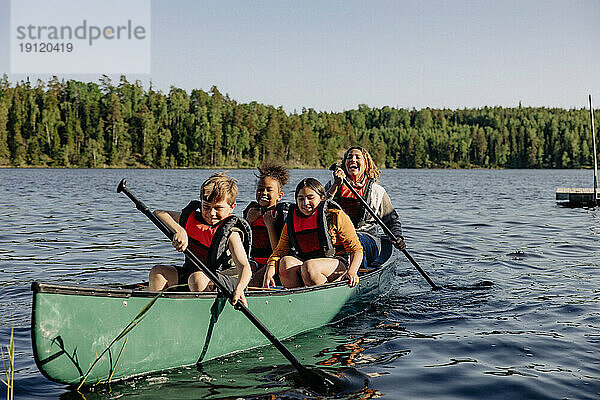 Betreuer und Kinder paddeln auf dem See gegen den Himmel im Sommercamp