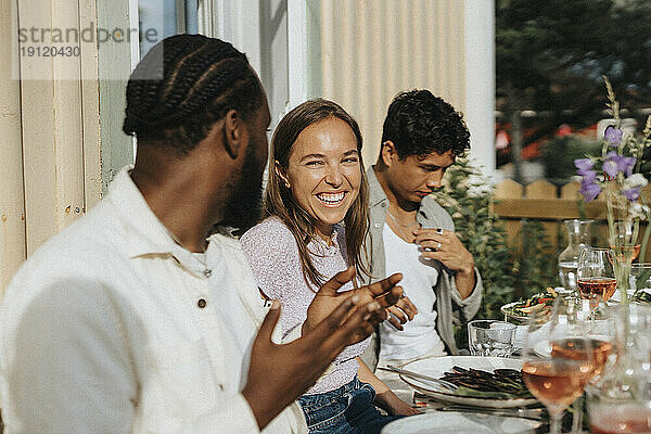 Glückliche junge Frau  die einen männlichen Freund ansieht  der sich während einer Dinnerparty im Café unterhält