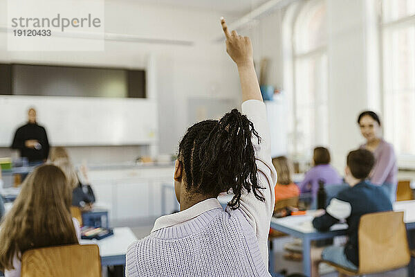 Rückansicht einer Studentin  die während einer Vorlesung im Klassenzimmer die Hand hebt