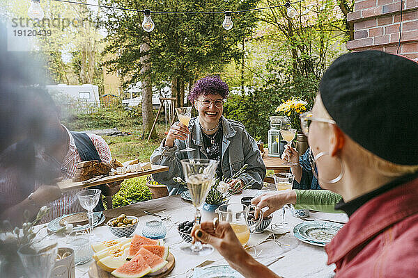 Lächelnde nicht-binäre Person genießt mit Freunden während einer Dinnerparty im Hinterhof
