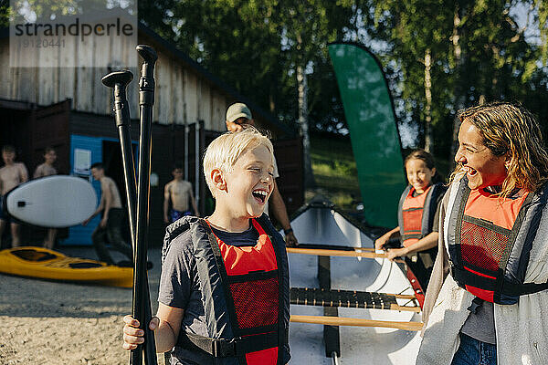 Glücklicher Junge mit Betreuer  der Schwimmwesten trägt  während er im Sommerlager Kajak fährt