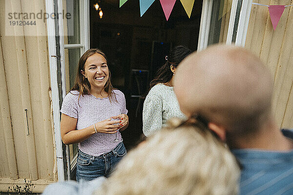 Glückliche Frau hält ein Weinglas in der Hand  während sie mit Freunden in einem Café zu Abend isst