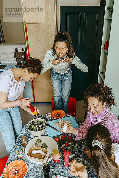 Hohe Winkelansicht einer Frau  die Freunde beim Mittagessen zu Hause fotografiert