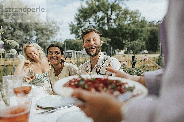 Glückliche männliche und weibliche Freunde lachen  während sie bei einer Dinnerparty am Tisch sitzen