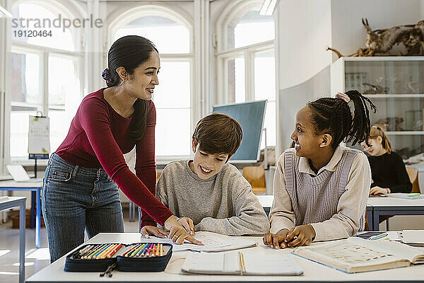 Glückliche Lehrerin  die eine Schülerin ansieht  während sie im Klassenzimmer assistiert