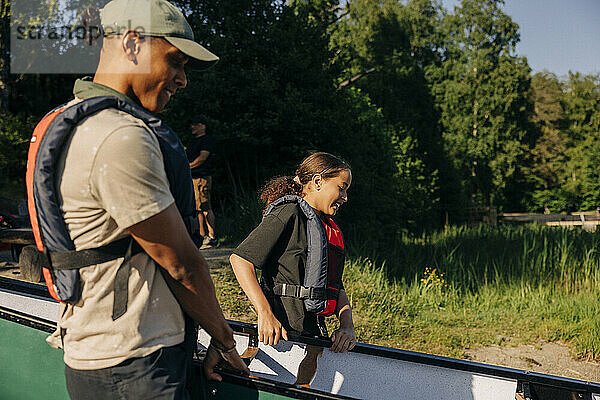 Betreuer und Mädchen tragen Kajak im Sommerlager