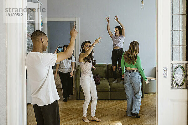 Junger Mann fotografiert tanzende Freundinnen im heimischen Wohnzimmer
