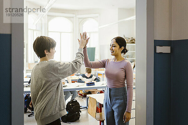 Eine lächelnde Lehrerin gibt einem Schüler im Klassenzimmer ein High-Five