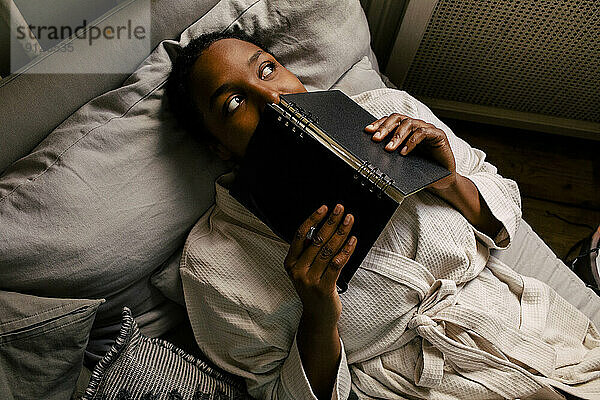 Hohe Winkel Ansicht der nachdenklichen Frau mit Buch auf dem Bett liegend zu Hause