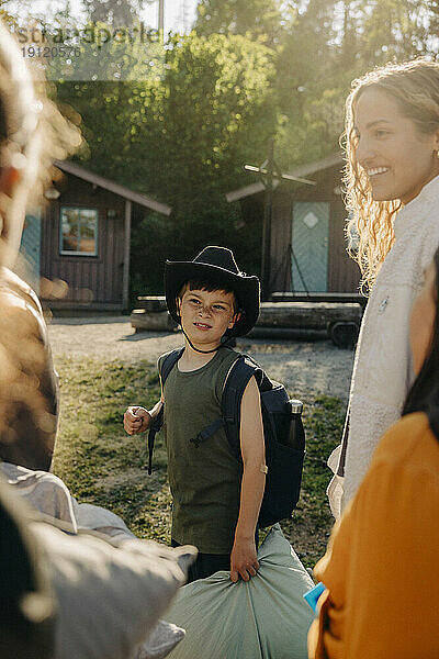 Junge mit Hut und Rucksack steht mit Freunden im Sommerlager