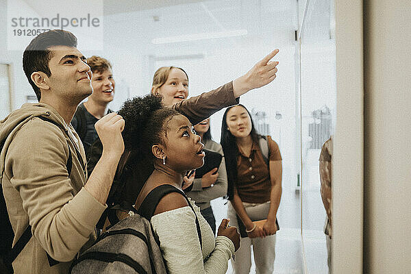 Männliche und weibliche Studenten verschiedener Rassen prüfen ihre Ergebnisse am schwarzen Brett in der Universität