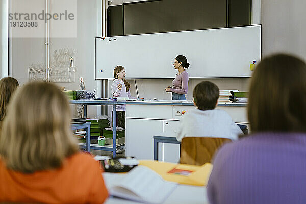 Lehrer steht und spricht mit einer Schülerin in der Nähe des Whiteboards im Klassenzimmer