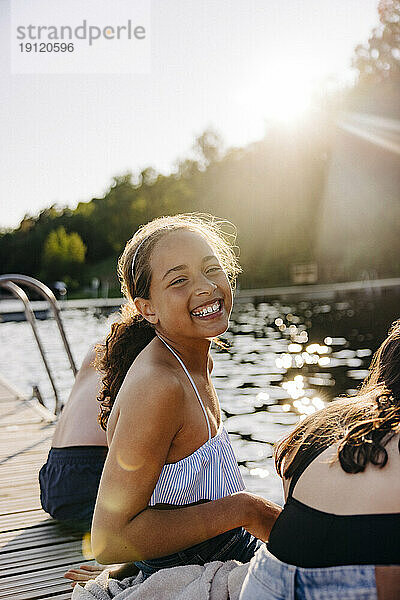 Seitenansicht Porträt von glücklichen Mädchen lachen  während mit Freunden auf Steg in der Nähe von See sitzen