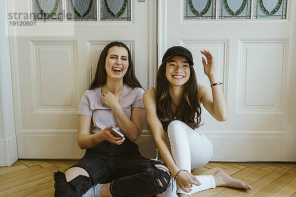 Glückliche junge Frauen  die zu Hause vor einer weißen Tür sitzen