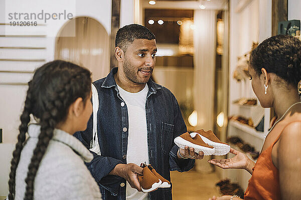 Mann hält Schuhe an seiner Tochter und spricht mit einer Verkäuferin in einer Boutique