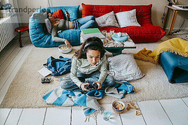 Hohe Winkel Ansicht der Frau spielt Videospiel  während Freund mit Smartphone auf Sofa zu Hause