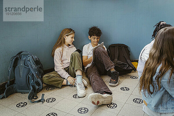 Junge und Mädchen lernen zusammen  während sie in der Nähe der Wand im Schulgebäude sitzen
