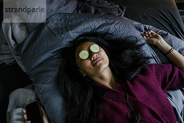 Hohe Winkel Ansicht der Frau auf dem Bett liegend mit Gurkenscheiben auf die Augen
