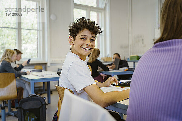 Seitenansicht Porträt eines lächelnden Schuljungen sitzt am Schreibtisch im Klassenzimmer