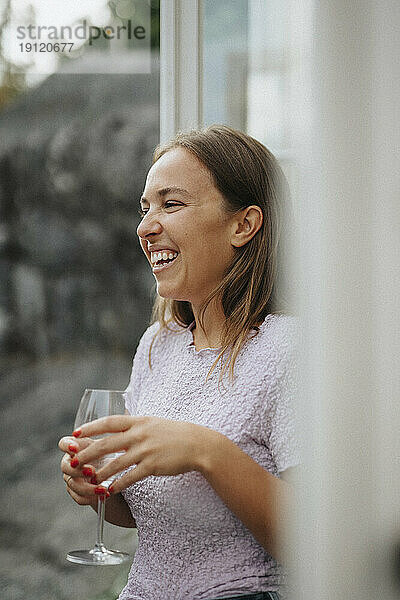 Glückliche Frau lacht und hält ein Weinglas während einer Dinnerparty im Café