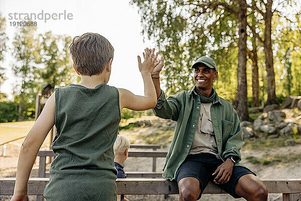 Rückansicht eines Jungen  der einem männlichen Betreuer im Sommercamp ein High Five gibt