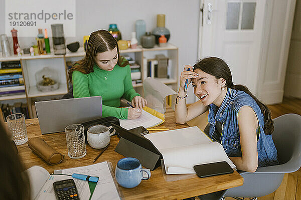 Lächelnde junge Frau  die bei ihrem Freund sitzt und zu Hause lernt