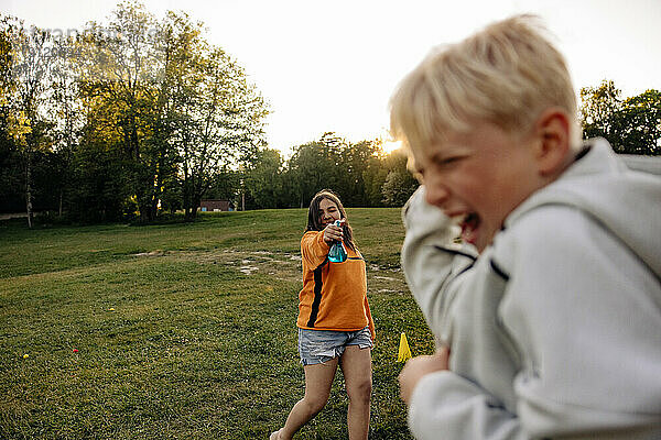 Mädchen bespritzt männlichen Freund beim Spielen auf dem Spielplatz im Ferienlager mit Wasser