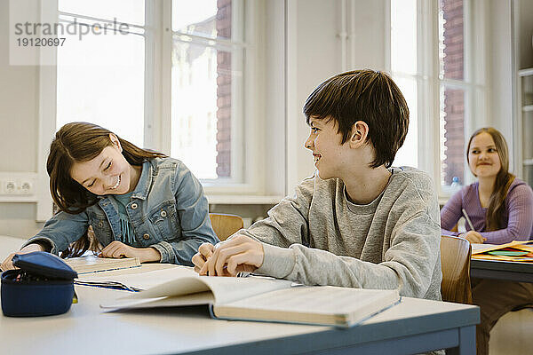 Glücklicher Junge lacht  während seine Freundin am Schreibtisch im Klassenzimmer sitzt