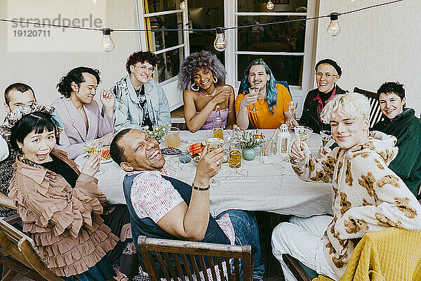 Hochformatige Ansicht von Freunden aus der LGBTQ-Gemeinschaft  die während einer Dinnerparty im Hinterhof mit Getränken posieren