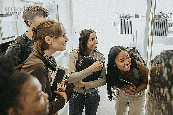 Fröhliche Studentinnen und Studenten verschiedener Rassen  die ihre Ergebnisse am schwarzen Brett in der Universität überprüfen