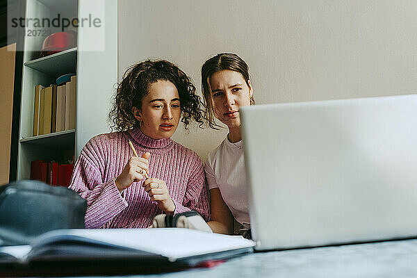 Junge Freundinnen schauen auf den Laptop  während sie gemeinsam Hausaufgaben machen