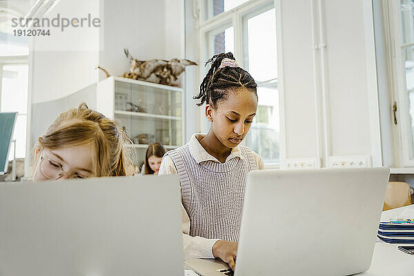 Schülerin mit Laptop auf dem Schreibtisch im Klassenzimmer