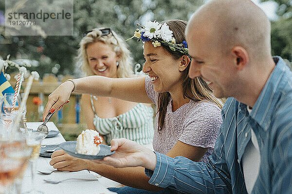 Glückliche junge Frau  die eine Tiara trägt  während sie einem männlichen Freund während einer Dinnerparty im Café Kuchen serviert