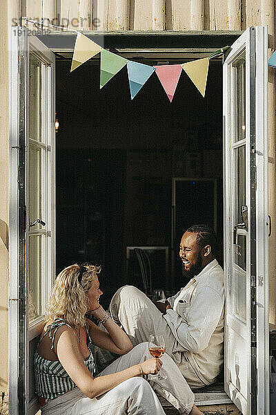 Glückliche männliche und weibliche Freunde genießen zusammen  während sie am Eingang eines Cafés sitzen