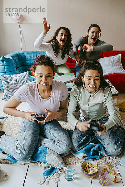 Fröhliche multirassische Freundinnen spielen ein Videospiel im Wohnzimmer zu Hause