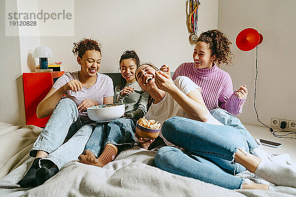 Fröhliche Freundinnen sehen fern  während sie zu Hause Snacks genießen