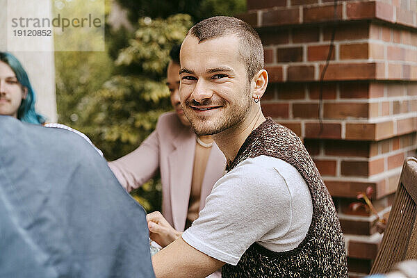 Seitenansicht Porträt von lächelnden Homosexuell Mann sitzt mit Freunden während der Party im Hinterhof