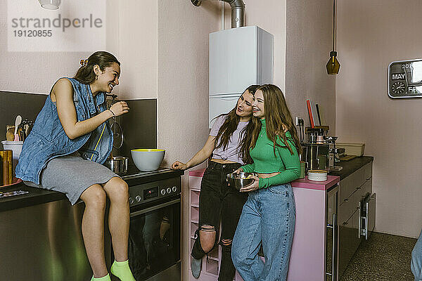 Lächelnde junge Freundinnen unterhalten sich in der Küche zu Hause