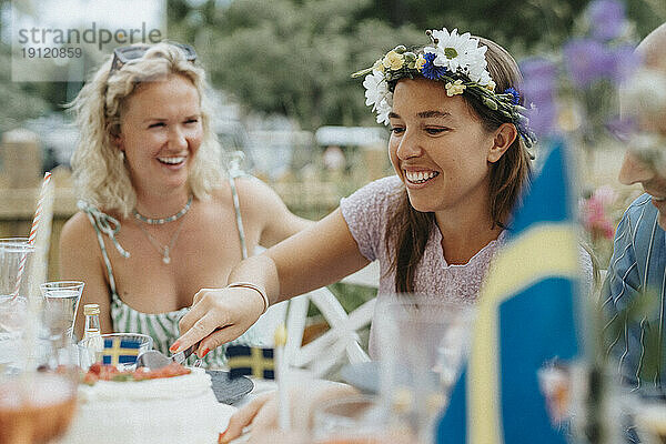 Lächelnde Frau schneidet Kuchen mit Freunden während einer Dinnerparty im Café an