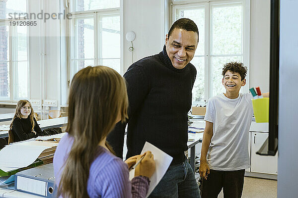 Glücklicher männlicher Lehrer  der sich mit den Schülern amüsiert  während er im Klassenzimmer unterrichtet