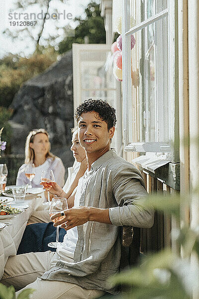 Porträt eines lächelnden jungen Mannes mit einem Weinglas in der Hand während einer Dinnerparty im Café