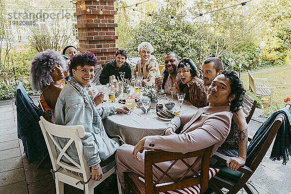 Porträt von glücklichen Freunden aus der LGBTQ-Gemeinschaft  die während einer Dinnerparty im Hinterhof am Esstisch sitzen