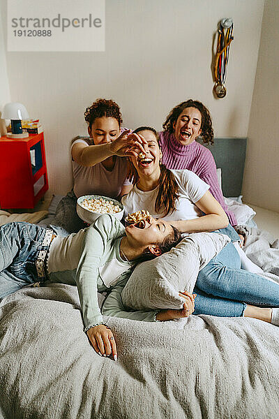 Verspielte Freundinnen sehen fern  während sie zu Hause Snacks genießen