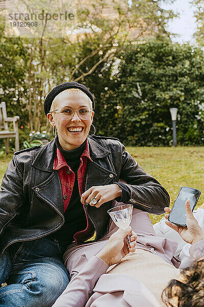 Porträt einer glücklichen schwulen Frau mit Lederjacke  die mit einem Freund im Hinterhof sitzt