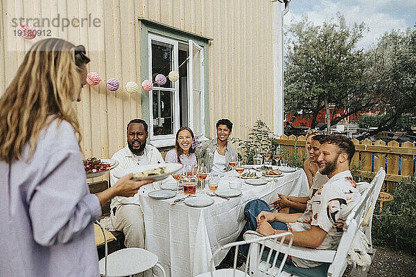 Frau serviert Essen an männliche und weibliche Freunde während einer Dinnerparty im Café