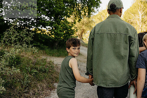 Porträt eines Jungen  der die Hand eines Betreuers hält  während er auf einem Fußweg im Ferienlager geht