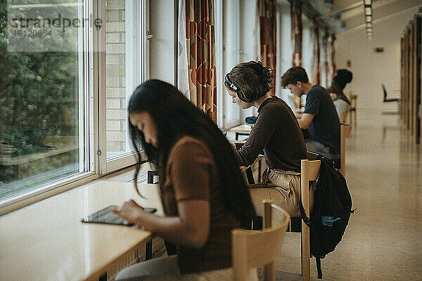 Seitenansicht einer jungen Frau mit Kopfhörern  die in der Bibliothek einer Universität lernt