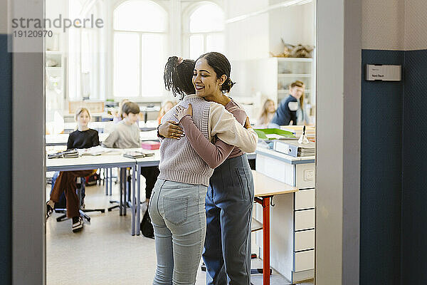 Schulmädchen  das eine Lehrerin umarmt  die im Klassenzimmer steht