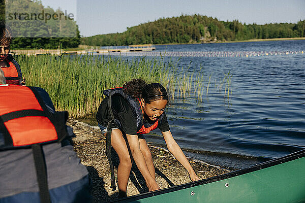 Mädchen trägt Schwimmweste und hält Kajak in der Nähe des Sees im Sommercamp